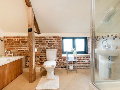 A bathroom with a toilet a bathtub a sink a glass shower enclosure and a wooden beam with exposed brick walls at Snipe in Wheatacre
