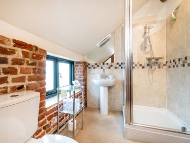 A bathroom with toilet sink glass shelf and shower with tiled walls at Snipe in Wheatacre