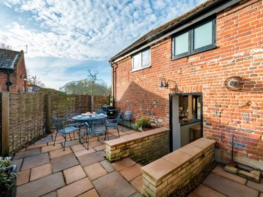 A patio with a metal table and chairs set next to a red brick building at Snipe in Wheatacre