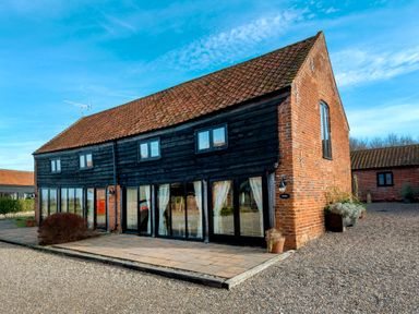 An exterior view of a two story building with red brick and black wooden walls and a tiled roof at Snipe in Wheatacre