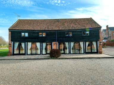 A building with black wooden cladding and multiple glass doors and windows at Snipe in Wheatacre