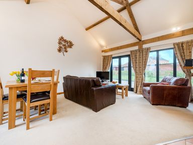 A living room with wooden dining table chairs brown leather sofas wall art and large windows with curtains at Pheasant in Wheatacre