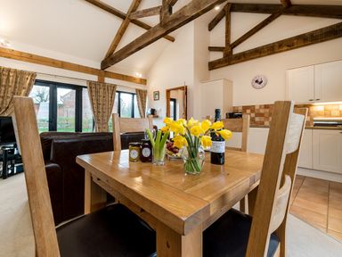 A wooden dining table with yellow flowers and condiments in a kitchen dining area with exposed ceiling beams at Pheasant in Wheatacre
