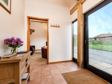 An entryway with a wooden cabinet with purple flowers and a room with sofas visible through a doorway at Pheasant in Wheatacre
