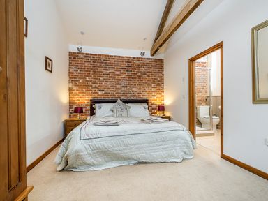 A bedroom with a double bed two bedside tables with lamps an exposed brick wall and an adjoining bathroom at Pheasant in Wheatacre