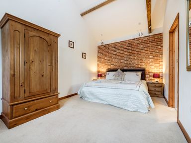 A bedroom with a bed against a brick wall a wooden wardrobe and bedside tables at Pheasant in Wheatacre