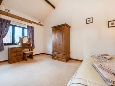 A bedroom with wooden wardrobe and dressing table with stool near a window at Pheasant in Wheatacre