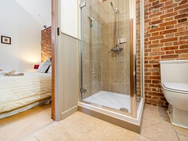 A bathroom with a shower cubicle and toilet next to a bedroom with a bed and bedside lamp at Pheasant in Wheatacre