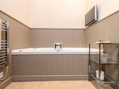 A bathroom with a corner bathtub towel rack and shelving unit with toiletries at Pheasant in Wheatacre