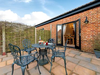 A patio with metal table and chairs outside a brick building with open doors at Pheasant in Wheatacre