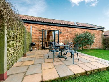 A patio with metal table and chairs outside a brick building with open doors and a barbecue grill at Pheasant in Wheatacre