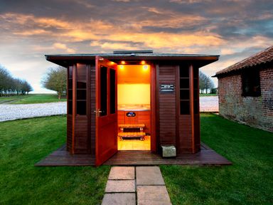 A wooden cabin with open doors showing an illuminated hot tub inside on grass at Pheasant in Wheatacre