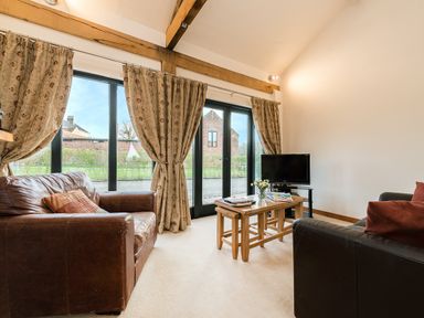 A living room with two leather sofas a small wooden coffee table and a television by glass doors with curtains at Partridge in Wheatacre