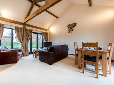 A living room with leather sofas a wooden dining table and chairs with curtains on windows at Partridge in Wheatacre