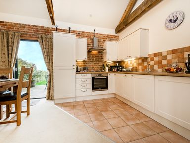 A kitchen with white cabinets tiled floor and wooden dining table near glass door at Partridge in Wheatacre