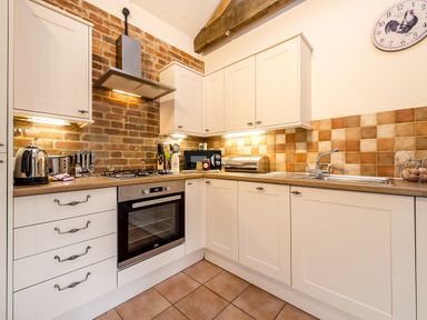A kitchen with white cabinets a brick wall tiled backsplash and various appliances at Partridge in Wheatacre