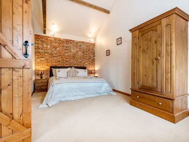 A bedroom with a bed against a brick wall and a wooden wardrobe at Partridge in Wheatacre