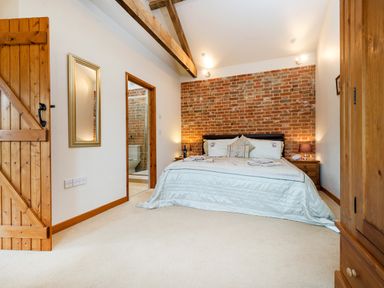 A bedroom with a bed, wooden door, mirror, exposed brick wall, and an en suite bathroom at Partridge in Wheatacre