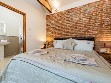 A bedroom with a bed towels and bedside tables beside a brick wall at Partridge in Wheatacre