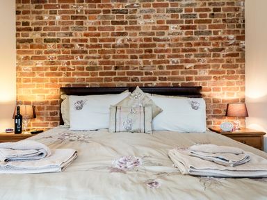 A bed with folded towels and pillows against a brick wall with bedside tables and lamps at Partridge in Wheatacre