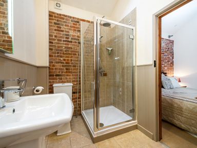 A bathroom with a glass shower enclosure sink and toilet next to a bedroom at Partridge in Wheatacre