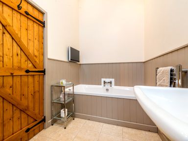 A bathroom with a wooden door a bathtub a small glass shelf and a towel rack at Partridge in Wheatacre