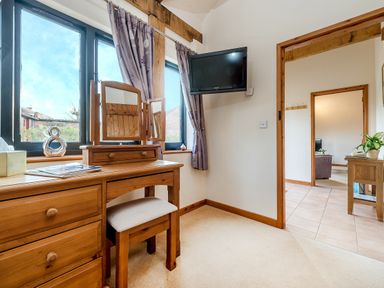 A room with a wooden dressing table and stool near windows with purple curtains and a wall-mounted TV at Partridge in Wheatacre