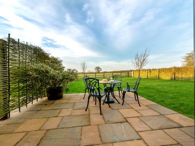 An outdoor patio with a round table and four chairs next to a green lawn and a wooden fence at Partridge in Wheatacre
