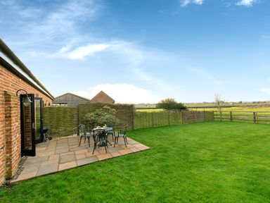 A patio area with table and chairs next to a brick house and a green lawn at Partridge in Wheatacre