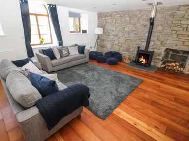 A living room with grey sofas a stone wall and a wood burning stove at Dalton Cottage in Llansaint