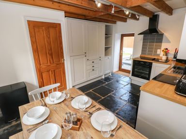 A kitchen with wooden ceiling beams a dining table set for four a door cabinets an oven and a sink at Dalton Cottage in Llansaint