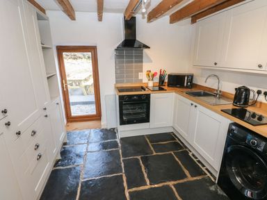 A kitchen with white cabinets wooden countertops a black oven stove microwave kettle and washing machine at Dalton Cottage in Llansaint