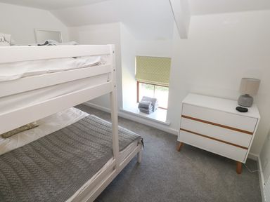 A bedroom with a white bunk bed a white dresser with a lamp and folded towels on the window sill at Dalton Cottage in Llansaint