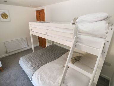 A small bedroom with white bunk beds a grey blanket on the lower bed a framed picture on the wall and a wooden door at Dalton Cottage in Llansaint