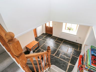 A hallway with stone tile floor wooden door wooden bench and a window with flowers at Dalton Cottage in Llansaint