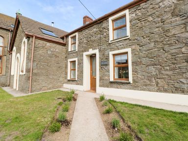A stone exterior of a house with multiple windows a wooden door and a pathway with small plants at Dalton Cottage in Llansaint