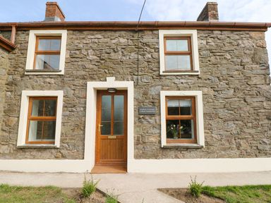 A stone cottage exterior with wooden door and windows at Dalton Cottage in Llansaint