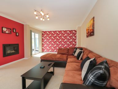 A living room with a brown sectional sofa black coffee table and patterned red wallpaper at Te Papa in North Petherton