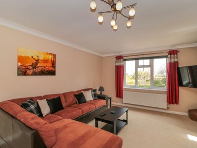 A living room with a sectional sofa and cushions a coffee table and a wall-mounted television at Te Papa in North Petherton