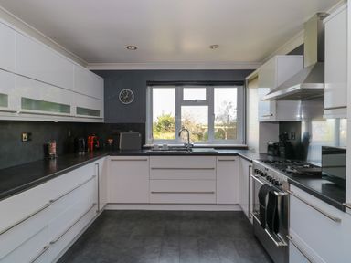 A kitchen with white cabinets black countertops a window above the sink and a stove with an extractor hood at Te Papa in North Petherton