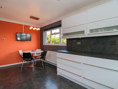 A kitchen with white cabinets black countertops a round table with four chairs and a wall mounted television at Te Papa in North Petherton