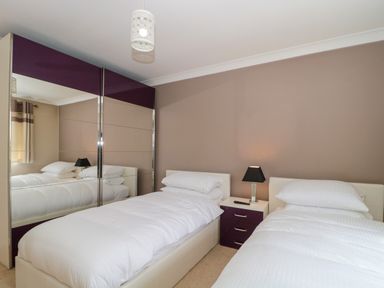 A bedroom with two single beds a nightstand with a lamp and a wardrobe with mirrored doors at Te Papa in North Petherton