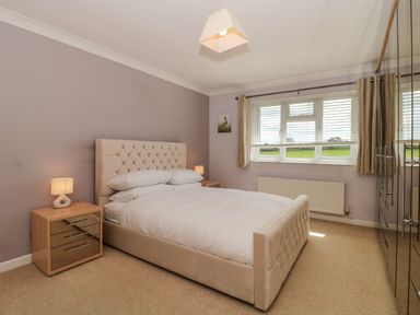 A bedroom with a double bed between two bedside tables with lamps and a window with curtains at Te Papa in North Petherton