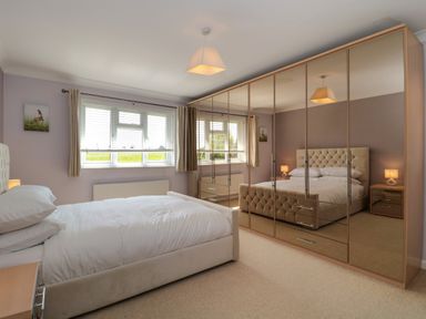 A bedroom with a double bed bedside tables lamps and mirrored wardrobes at Te Papa in North Petherton