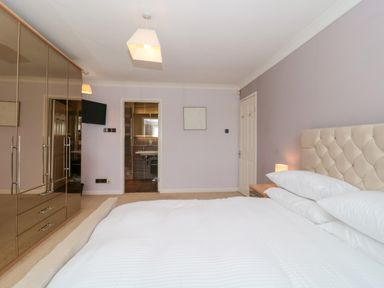 A bedroom with a bed white bedding a mirrored wardrobe a wall-mounted tv and an en suite bathroom at Te Papa in North Petherton