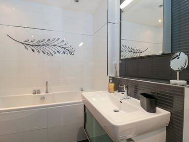 A bathroom with a bathtub a sink a mirror and wall decoration at Te Papa in North Petherton
