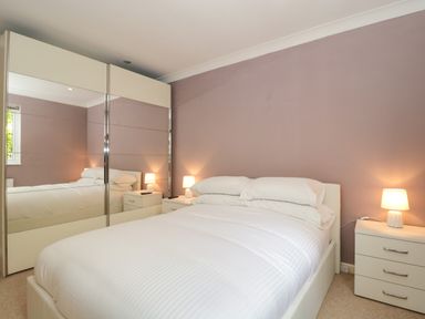 A bedroom with a bed white bedding bedside tables lamps and a wardrobe with mirrored doors at Te Papa in North Petherton