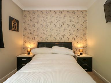 A bedroom with a bed with white bedding two bedside tables with lamps floral wallpaper and a wall painting at Te Papa in North Petherton
