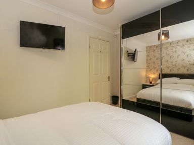 A bedroom with a bed a wall mounted television a door and a mirrored wardrobe at Te Papa in North Petherton