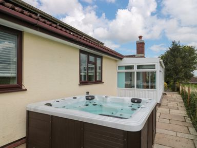 An outdoor hot tub next to a house with a tiled roof and windows and a paved pathway alongside the house at Te Papa in North Petherton